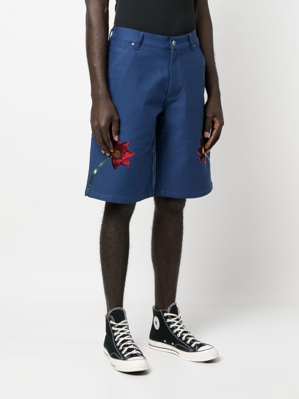 Model draagt de blauwe workwear short met zwarte top en hoge zwarte canvas sneakers