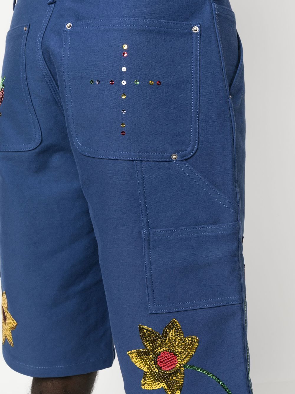 Detail van achterzak met kruis van losse pailletten, hamerlus en gereedschapszak