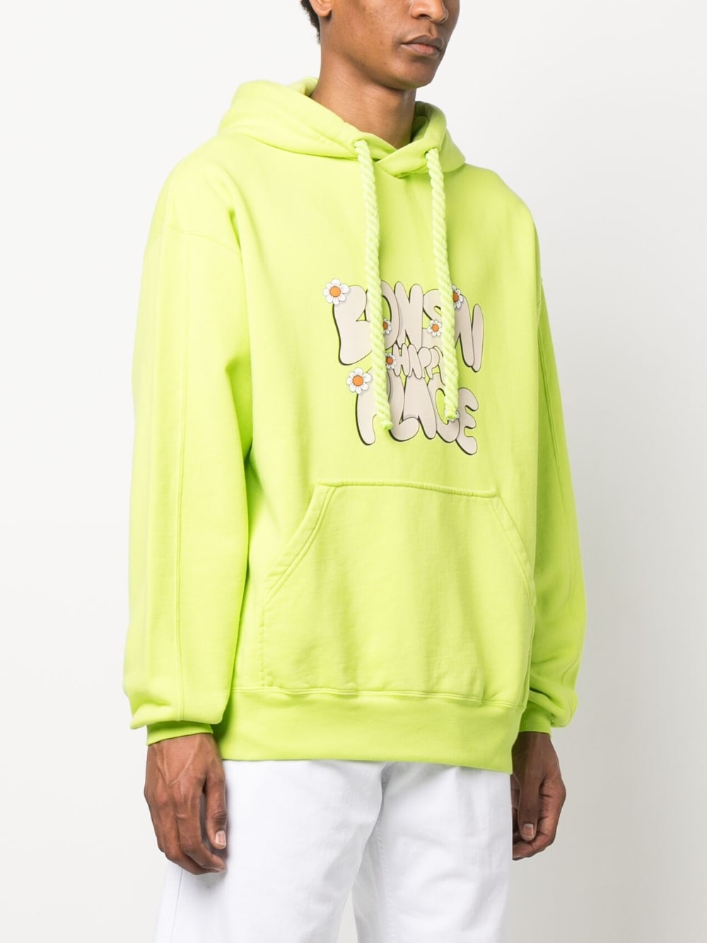 Model draagt de acid green hoodie met witte broek, ruime pasvorm zichtbaar
