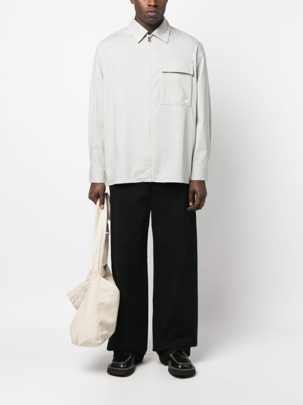 Model draagt het lichtgrijze overshirt over een zwarte broek, met canvas schoudertas
