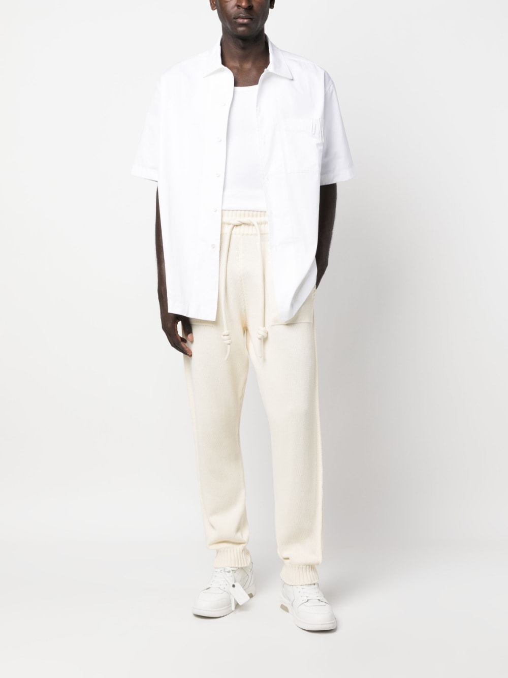 Model draagt de crèmekleurige trackpants met een wit overhemd, vooraanzicht