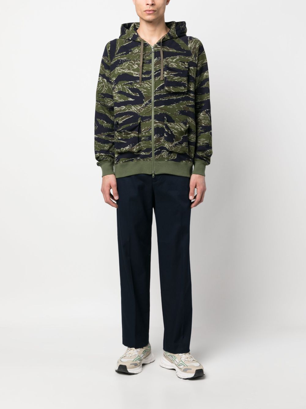 Model draagt de blauwe pantalon bij witte sneakers