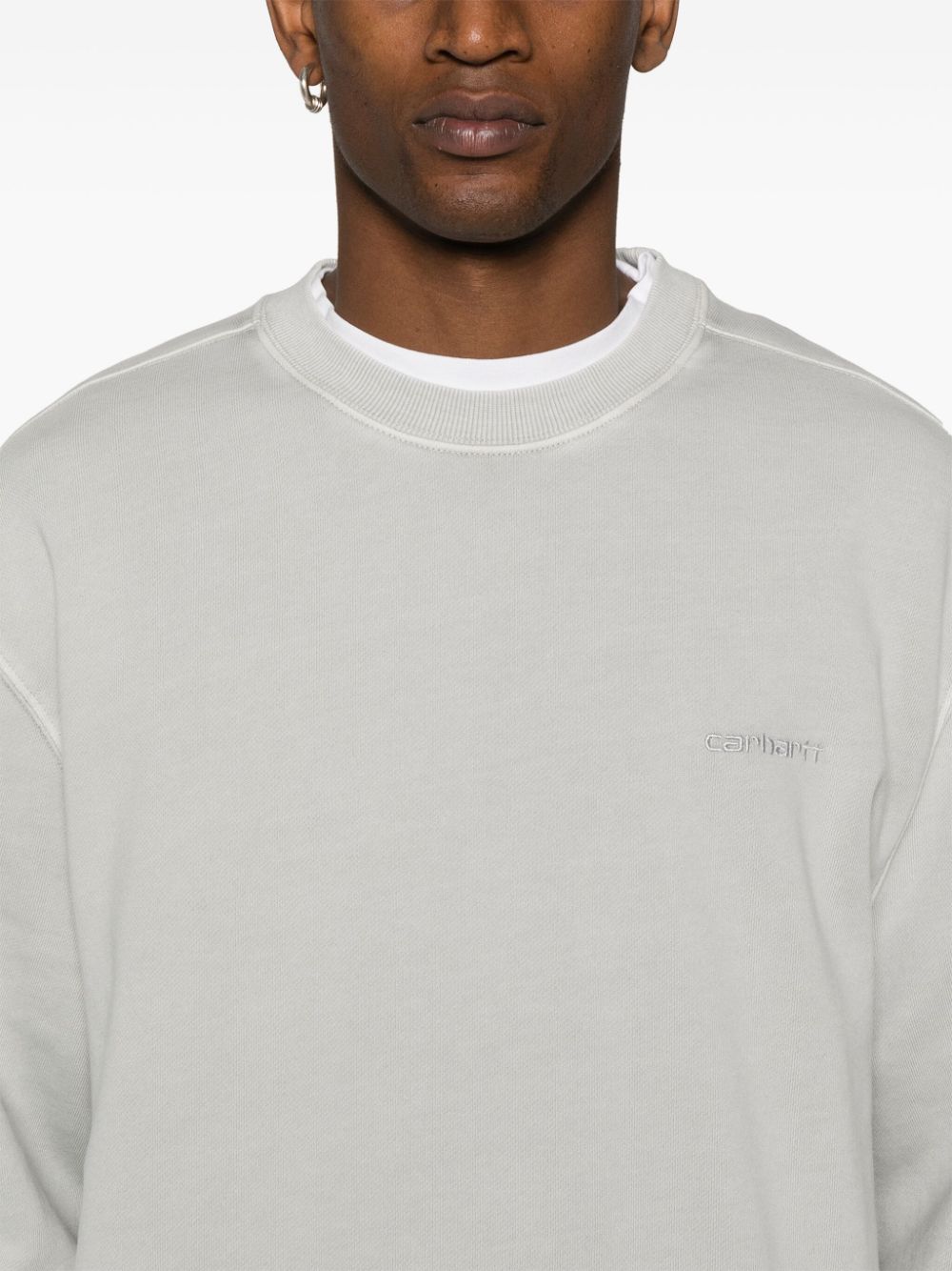 Detail van de geribde ronde hals met daaronder een wit T-shirt zichtbaar