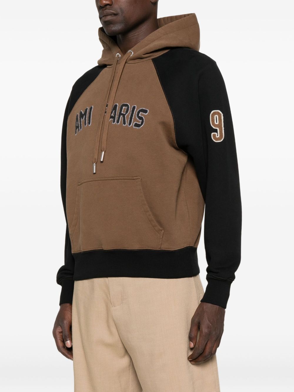 Zijaanzicht met de opgelegde 9 op de zwarte raglanmouw van de AMI Paris hoodie