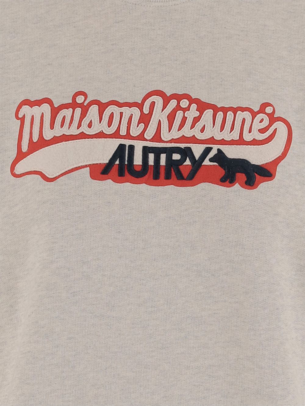 Detail van de opgelegde varsityapplicatie: crèmekleurig geborduurd Maison Kitsuné-schrift op rode banier met donkerblauw AUTRY-logo en vos