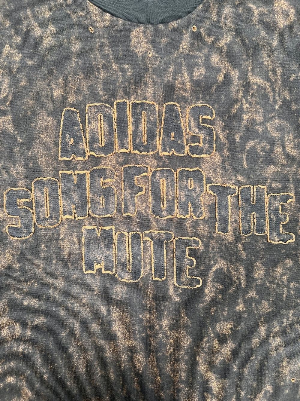 Close-up van de geborduurde belettering ADIDAS SONG FOR THE MUTE op de borst