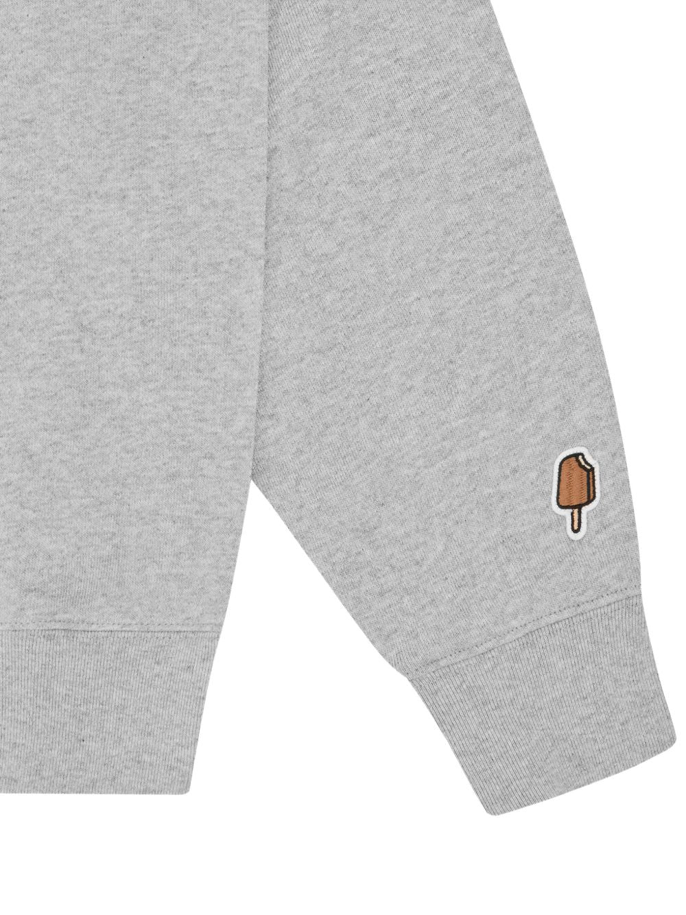 Mouwdetail met geborduurd ijsje boven de geribde manchet