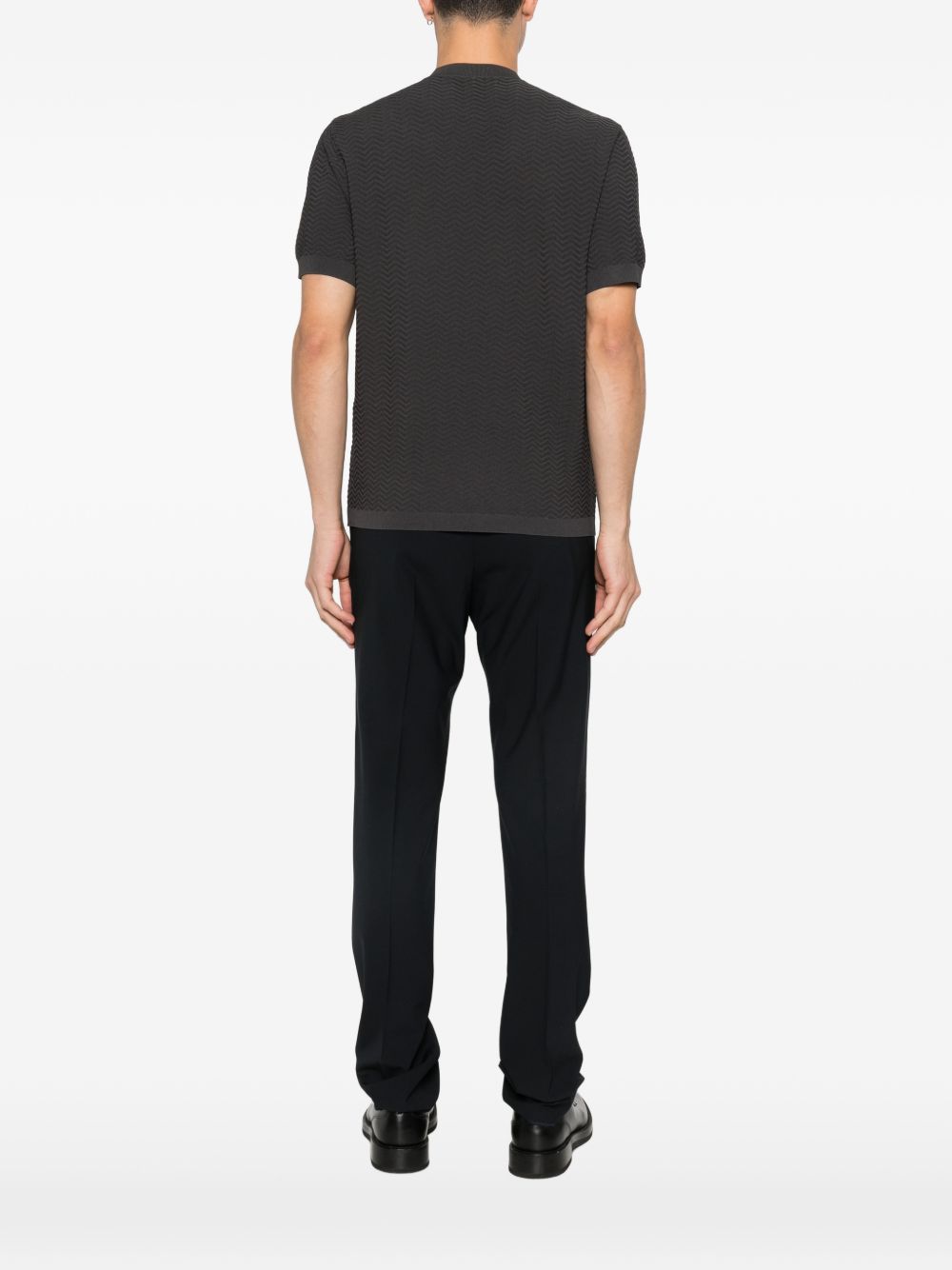 Achterzijde van het gebreide T-shirt op het model bij een donkere broek