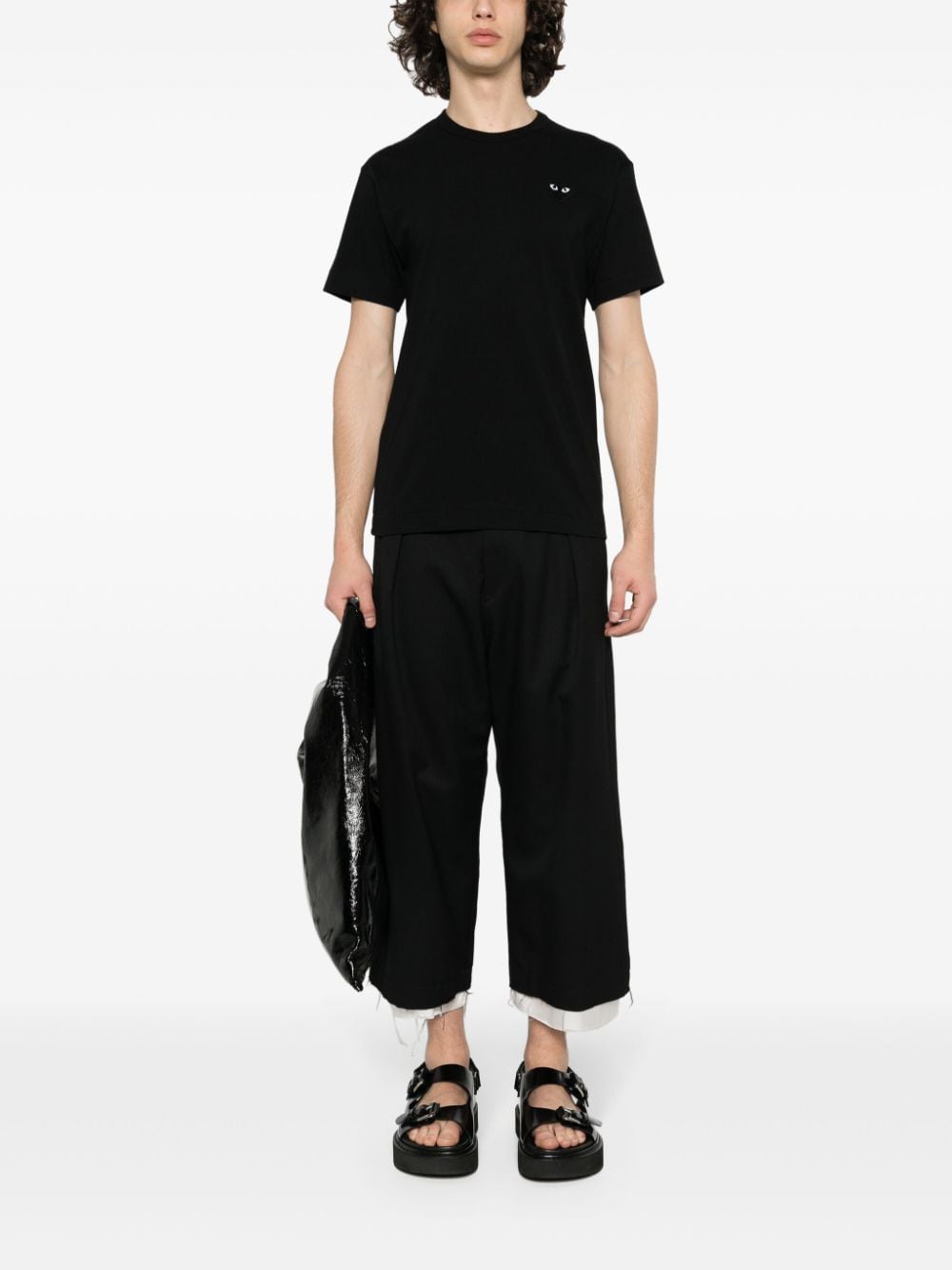 Het zwarte PLAY T-shirt gedragen bij een zwarte broek en sandalen