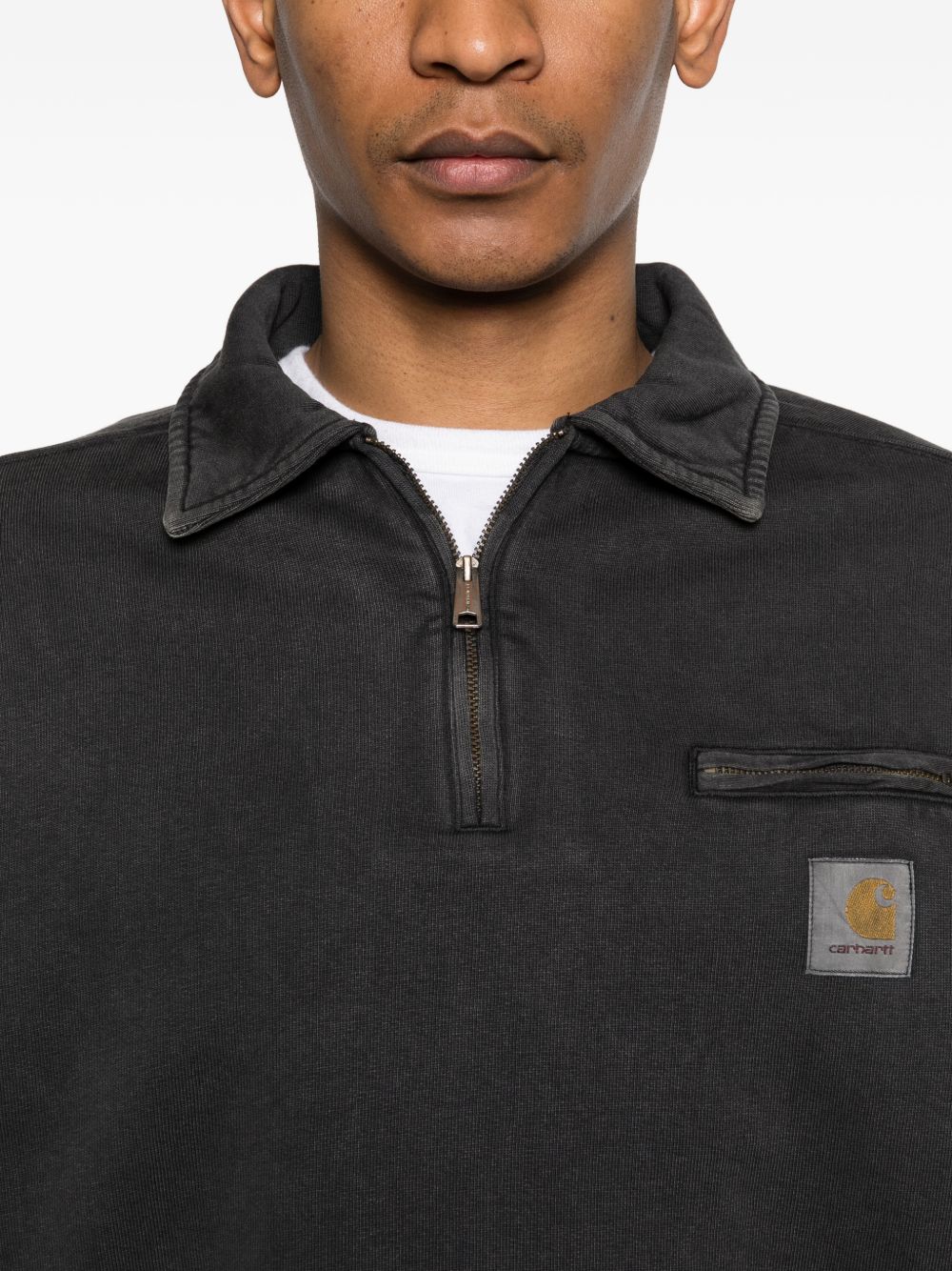 Detail van de halve rits, de omslagkraag en het geweven vierkante Carhartt-label op de borst