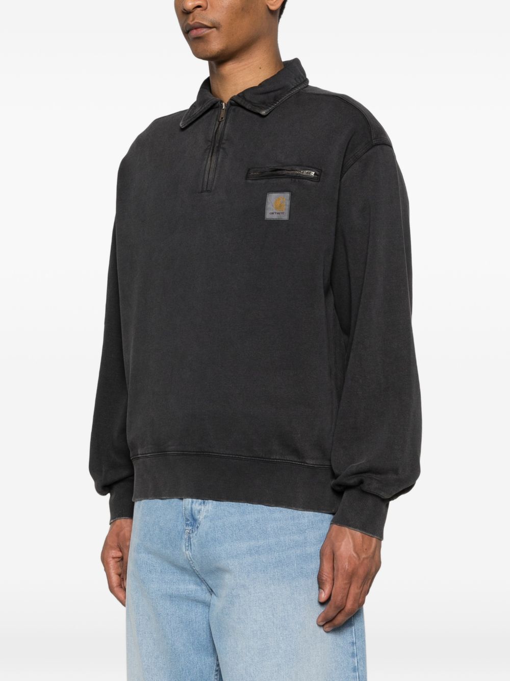 Model draagt de zwarte half-zip sweater van Carhartt WIP met de kraag open