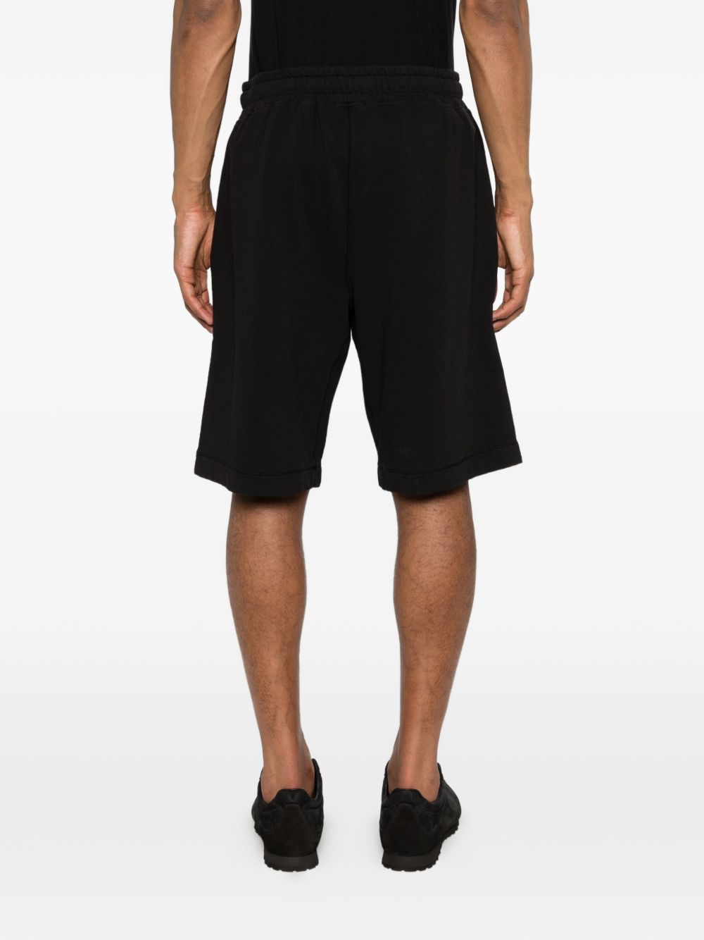 Model draagt de zwarte bermudashort van C.P. Company tot op de knie