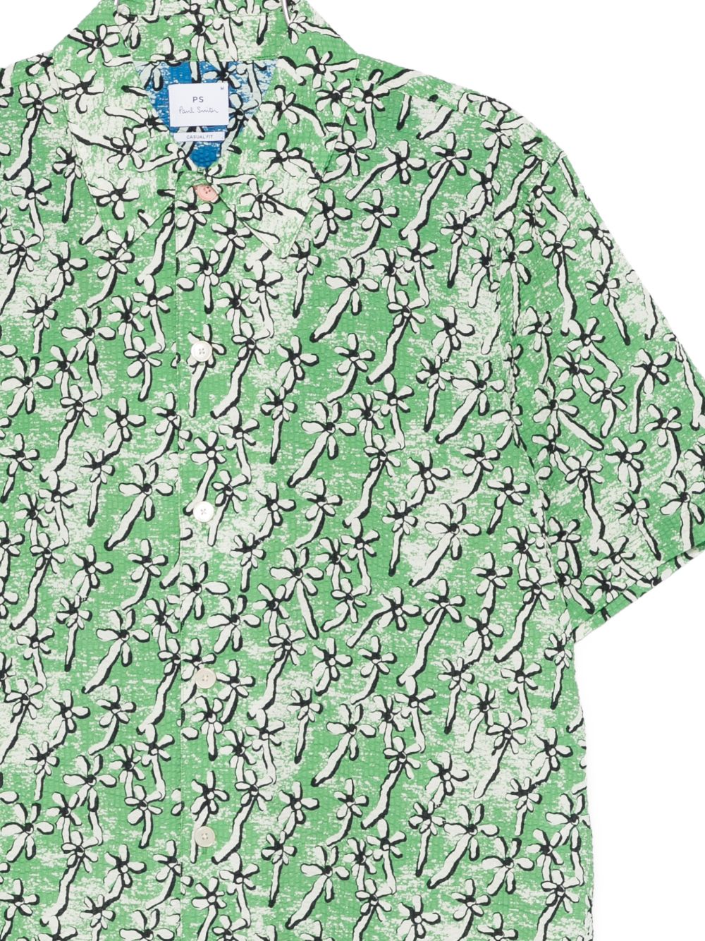 Detail van de seersuckerstructuur, de contrasterende bovenste knoop en de blauw gevoerde schouderpas