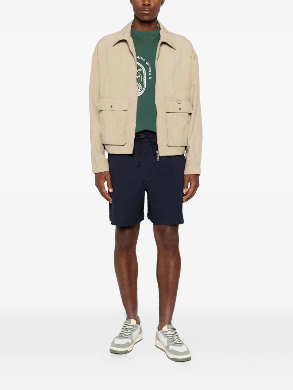 Volledige look met de marineblauwe Maison Kitsuné short, groen T-shirt en beige jack