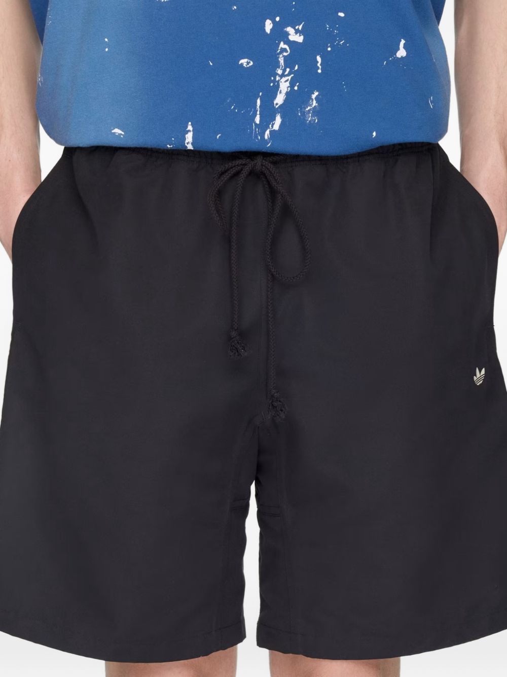 Model draagt de zwarte Adidas x Song For The Mute 007 short met blauw T-shirt