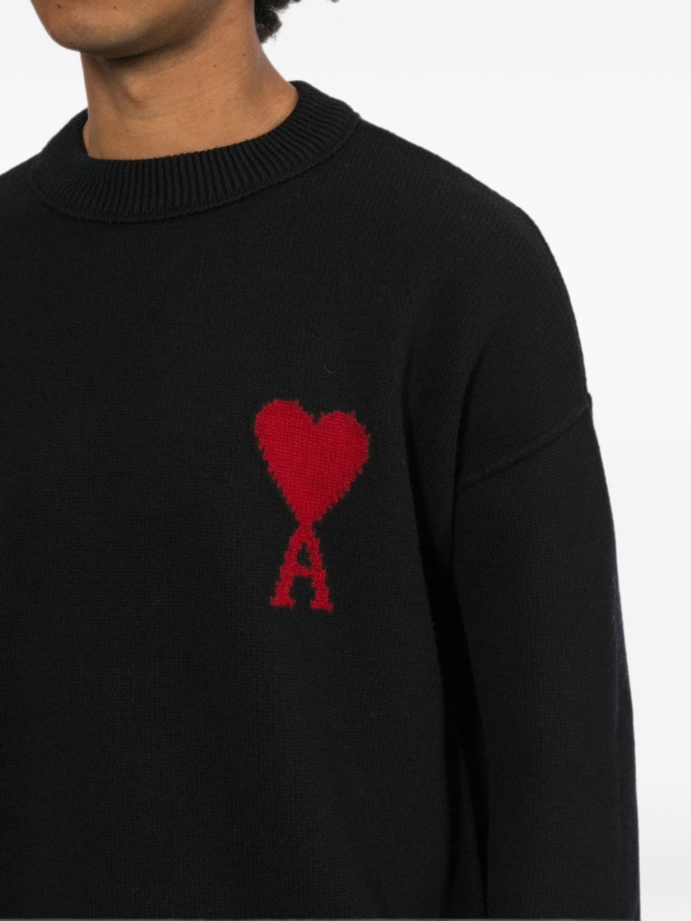 Close-up van de ronde hals en het rode intarsia Ami de Coeur logo op de AMI Paris trui