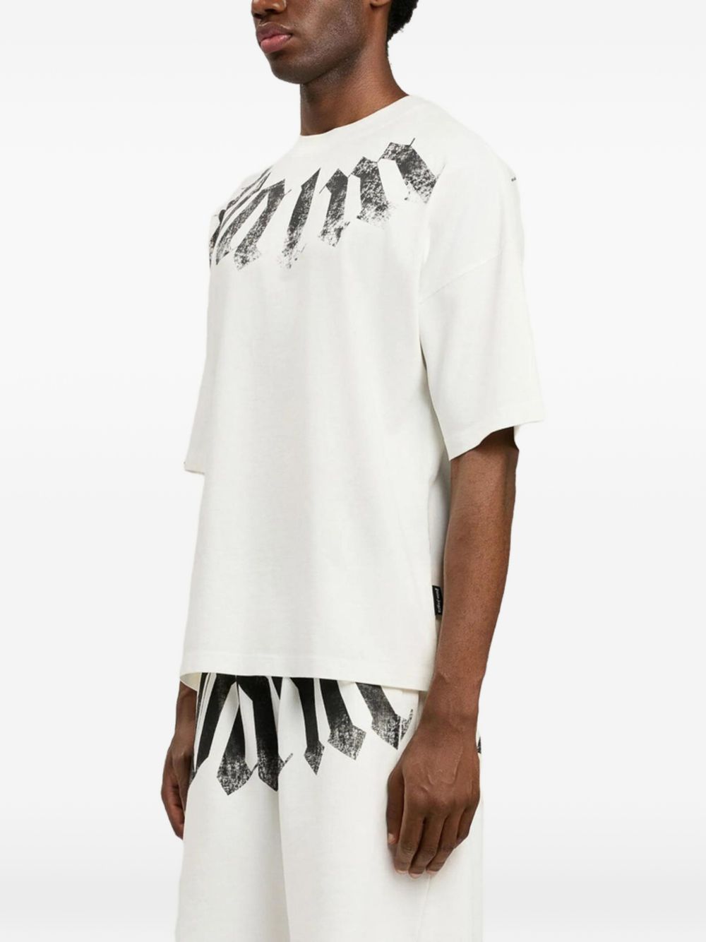 Model draagt het shirt van opzij, met de laag vallende schoudernaad zichtbaar