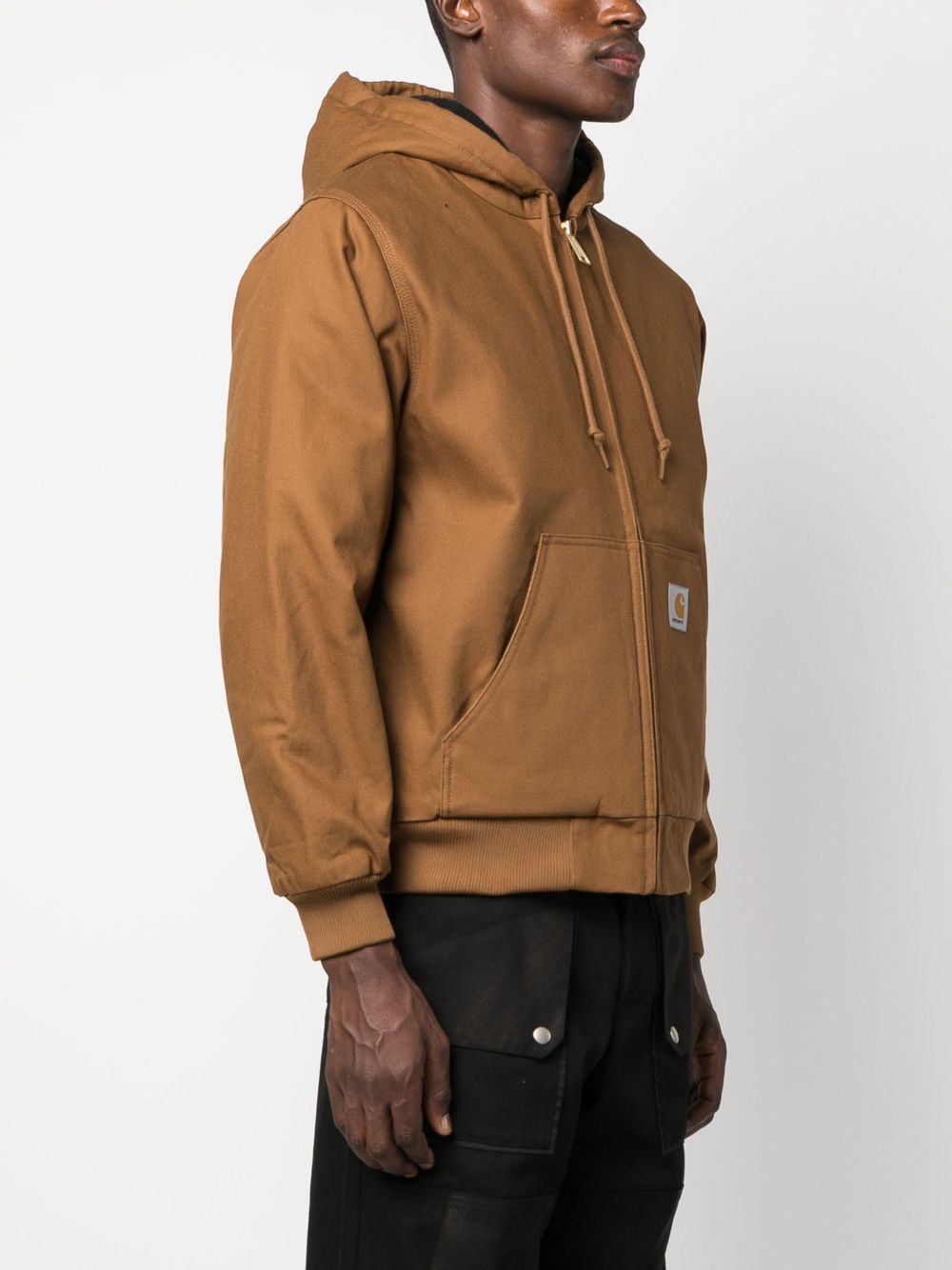 Zijaanzicht van de bruine Carhartt WIP Active Jacket met ingezette zijzak